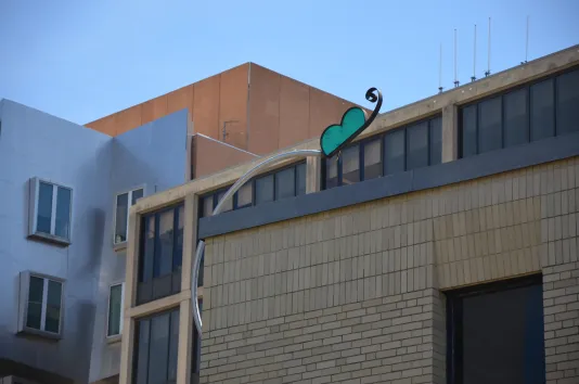 Glass and steel green butterfly mounted to the corner of a brick building.