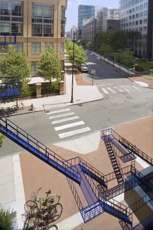 Blue sculpture made out of multiple ladder forms hangs over a street sidewalk and intersection.