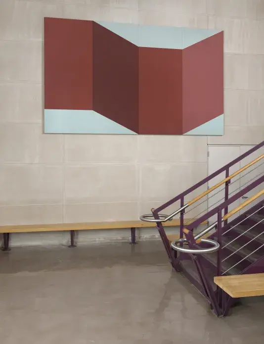 Large abstract painting comprised of maroon and light blue geometric shapes hanging on a cement wall above a wood staircase with purple painted railings.